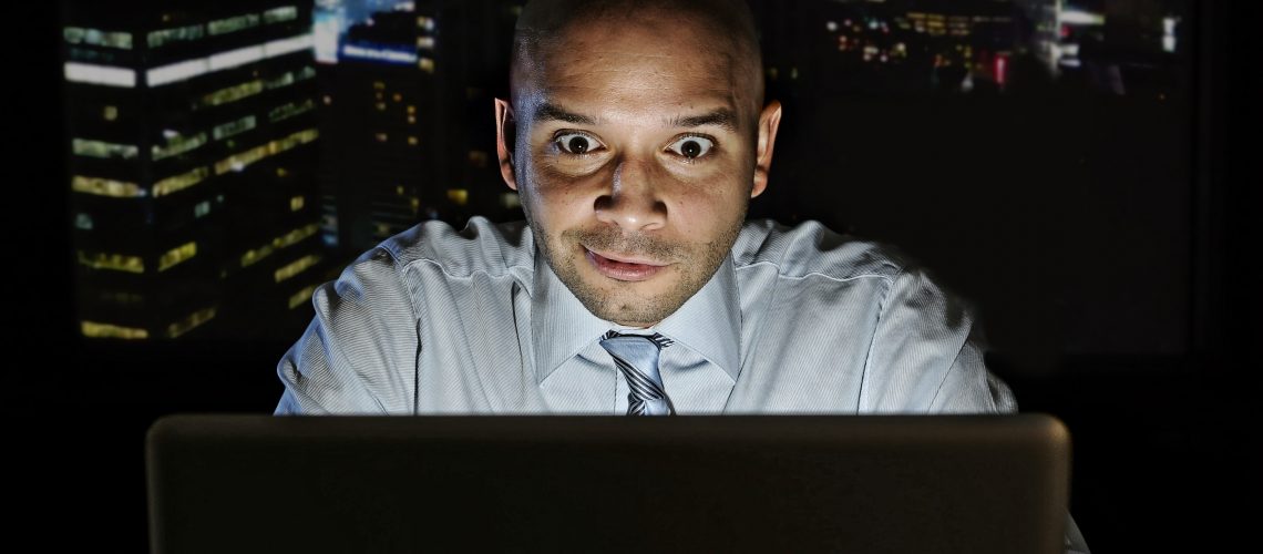 addict businessman alone at night sitting at office computer laptop watching porn, online gambling or working late in addiction concept